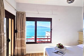 Ein Hotelzimmer mit Bett, Fenster mit Blick auf Meer und Berge sowie einem Vorhang.