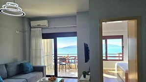 A modern living room with a sofa, a coffee table with a tray of pastries, a balcony with a table and chairs, and a view of the sea. - Albina Apartment 118 - Balcony & Sea View, Sarandë, Albania (Sarandë)