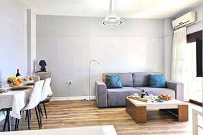 Una sala de estar moderna con un sofá gris, una mesa de centro y un comedor con mesa puesta para una comida.