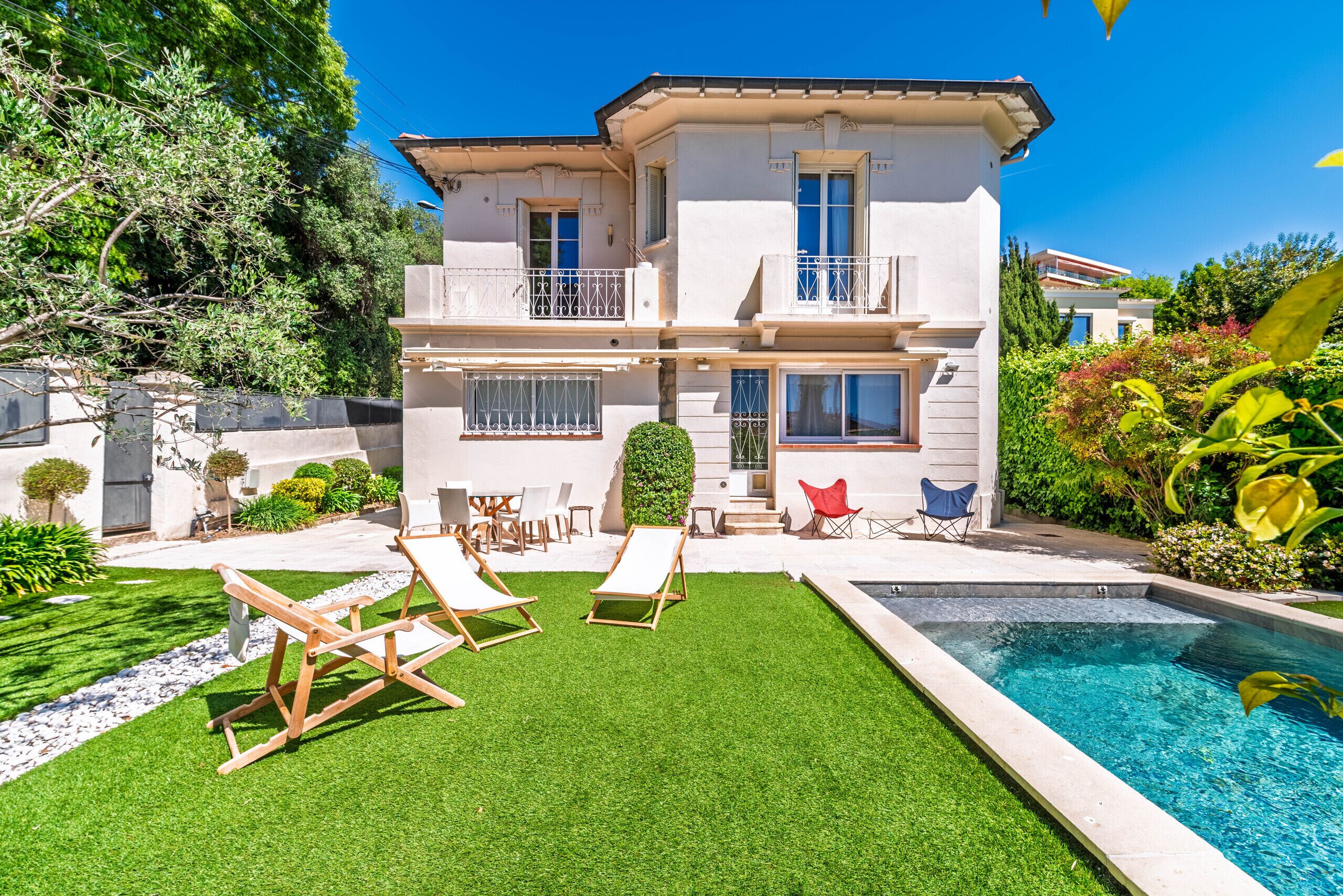 A two-story house with a swimming pool, outdoor seating, and a well-maintained garden.
