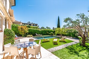 Un espace aménagé au bord de la piscine, avec une table et des chaises en verre, une petite piscine et une pelouse bien entretenue.