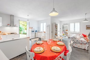 Een moderne keuken met witte kasten, een eethoek met een rode tafelkleed en een slaapkamer met bloemenbeddengoed.