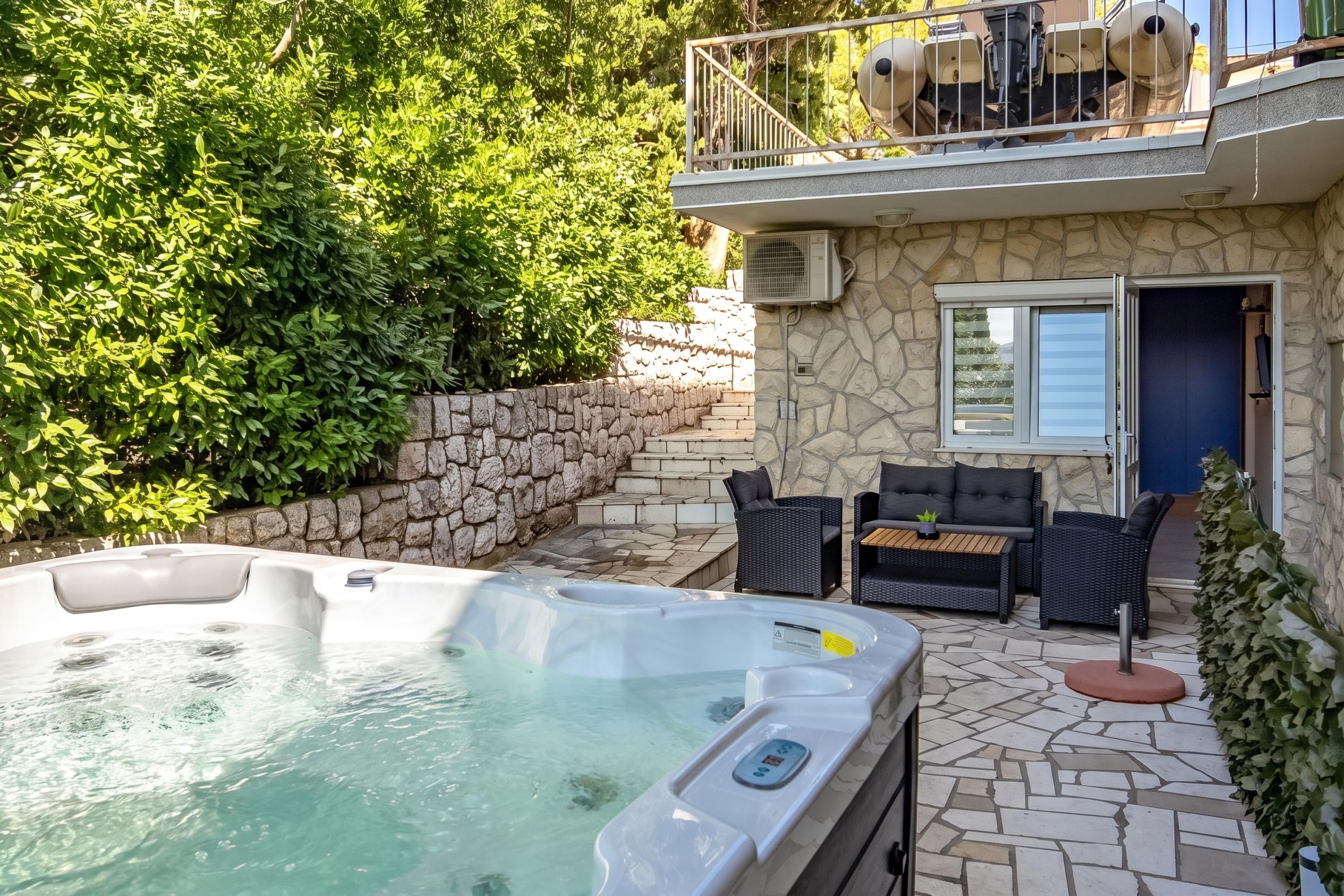 A hot tub with a control panel, a stone wall, and a patio with outdoor furniture.