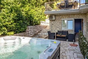Una bañera de hidromasaje con panel de control, pared de piedra y un patio con mobiliario exterior.