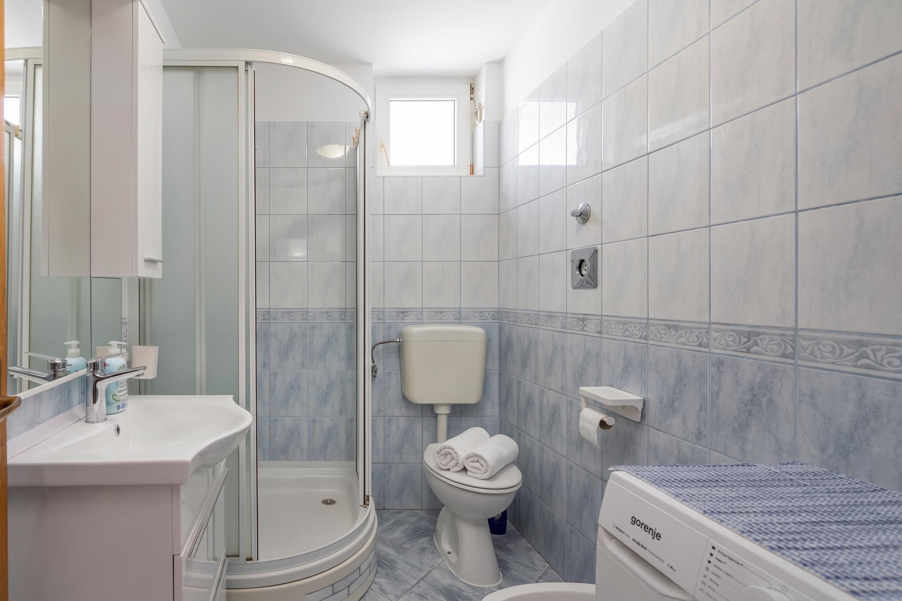 Un baño moderno con cabina de ducha de vidrio, inodoro con portarrollos y lavabo con espejo.