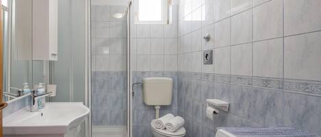 Un baño moderno con cabina de ducha de vidrio, inodoro con portarrollos y lavabo con espejo.