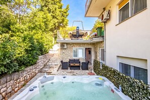 A hot tub in a backyard with stone walls, a patio with outdoor furniture, and a building with a balcony. - Seaview Apartment With Jacuzzi Ivano, Novi Vinodolski, Croatia (Novi Vinodolski)