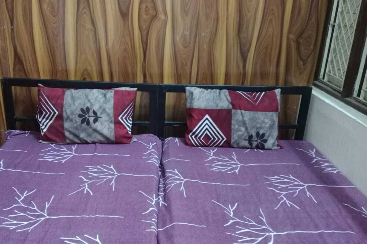 A bed with a purple bedspread featuring white tree branches, flanked by two pillows with geometric and floral patterns.