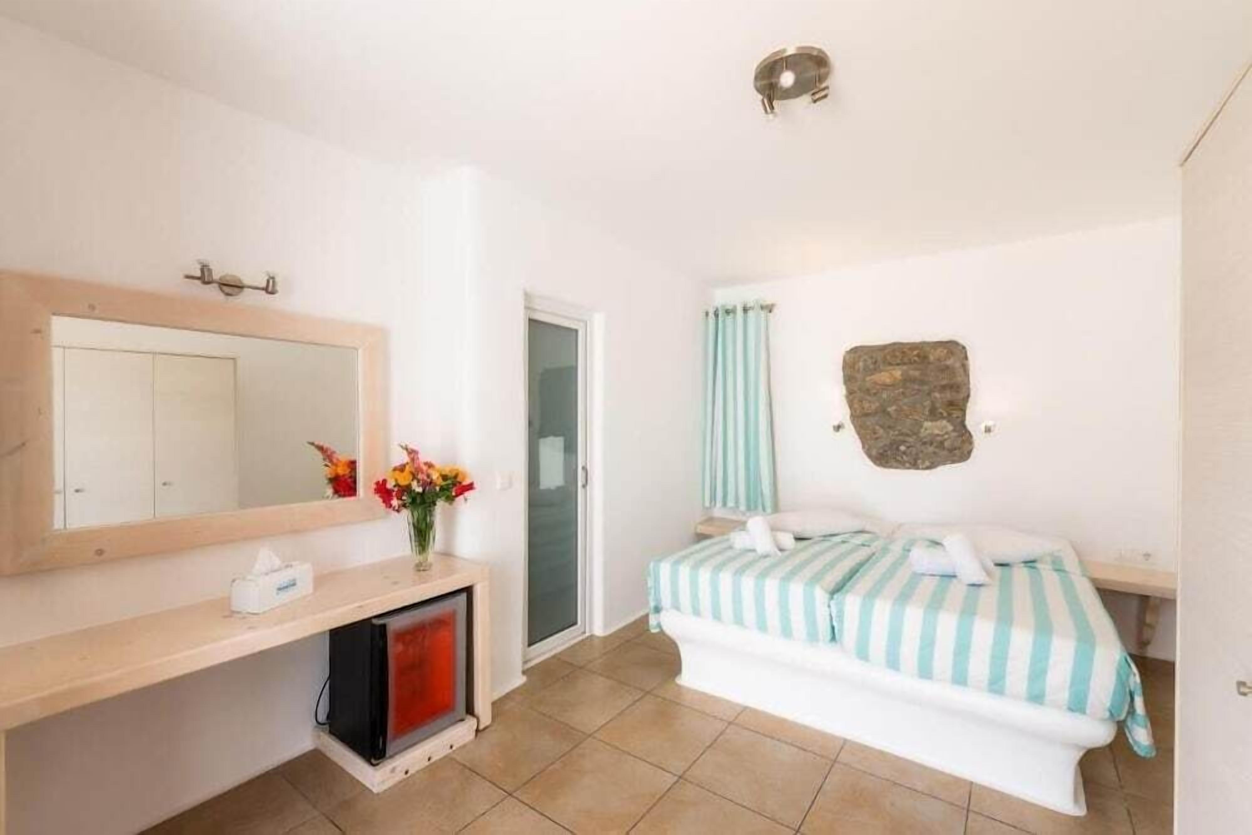 Un dormitorio con cama, mesita de noche, espejo, cómoda y puerta.