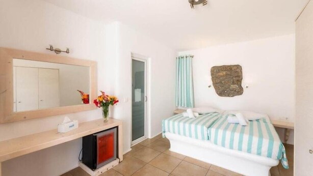 Un dormitorio con cama, mesita de noche, espejo, cómoda y puerta.