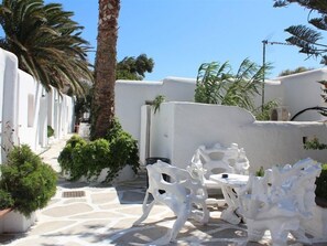 A white-walled outdoor area with a stone floor, white furniture, and greenery including palm trees and potted plants. - Paradise Beach Resort - Adults Only (Mykonos)