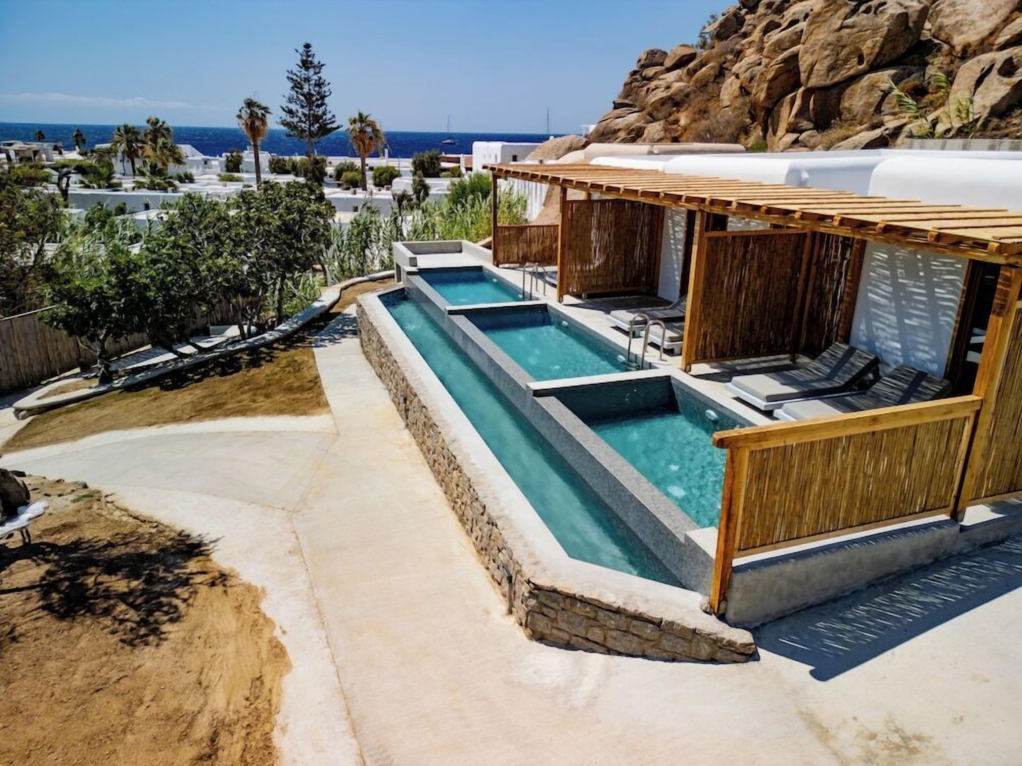 Uma área de piscina com várias piscinas retangulares, assentos com deck de madeira e vista para o oceano.