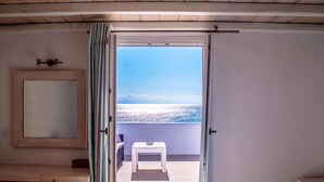 Una habitación con techo de madera, una mesa blanca y vista al mar a través de un puerta abierta.