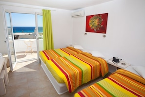 Habitación de hotel con dos camas, un balcón con vistas al mar, un equipo de aire acondicionado, un cuadro y un teléfono en la mesita de noche.