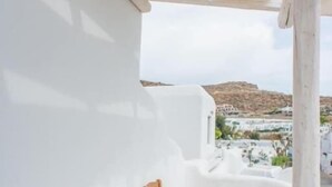 Un balcón con una mesa blanca y dos sillas de madera, con vistas a un pueblo de edificios blancos y una colina al fondo.