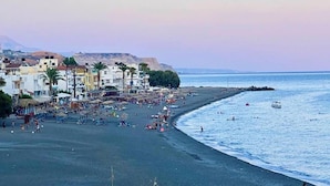 A beach with buildings, palm trees, and people.