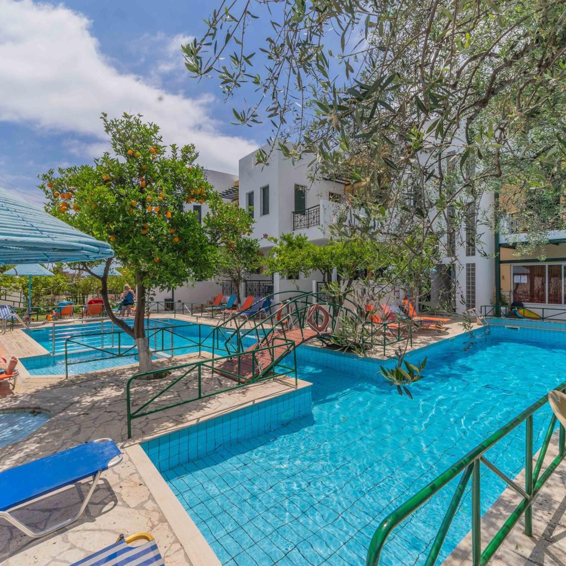 A swimming pool area with multiple pools, sun loungers, and a tree.
