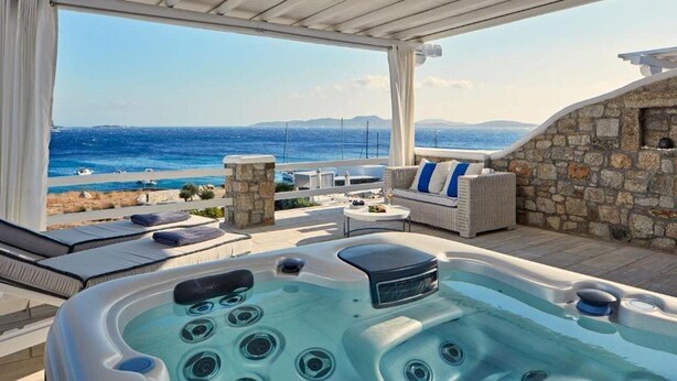 A hot tub with a view of the sea and mountains, a stone wall, and a seating area with cushions and a table. - Delight Boutique Hotel & Spa (Mykonos)