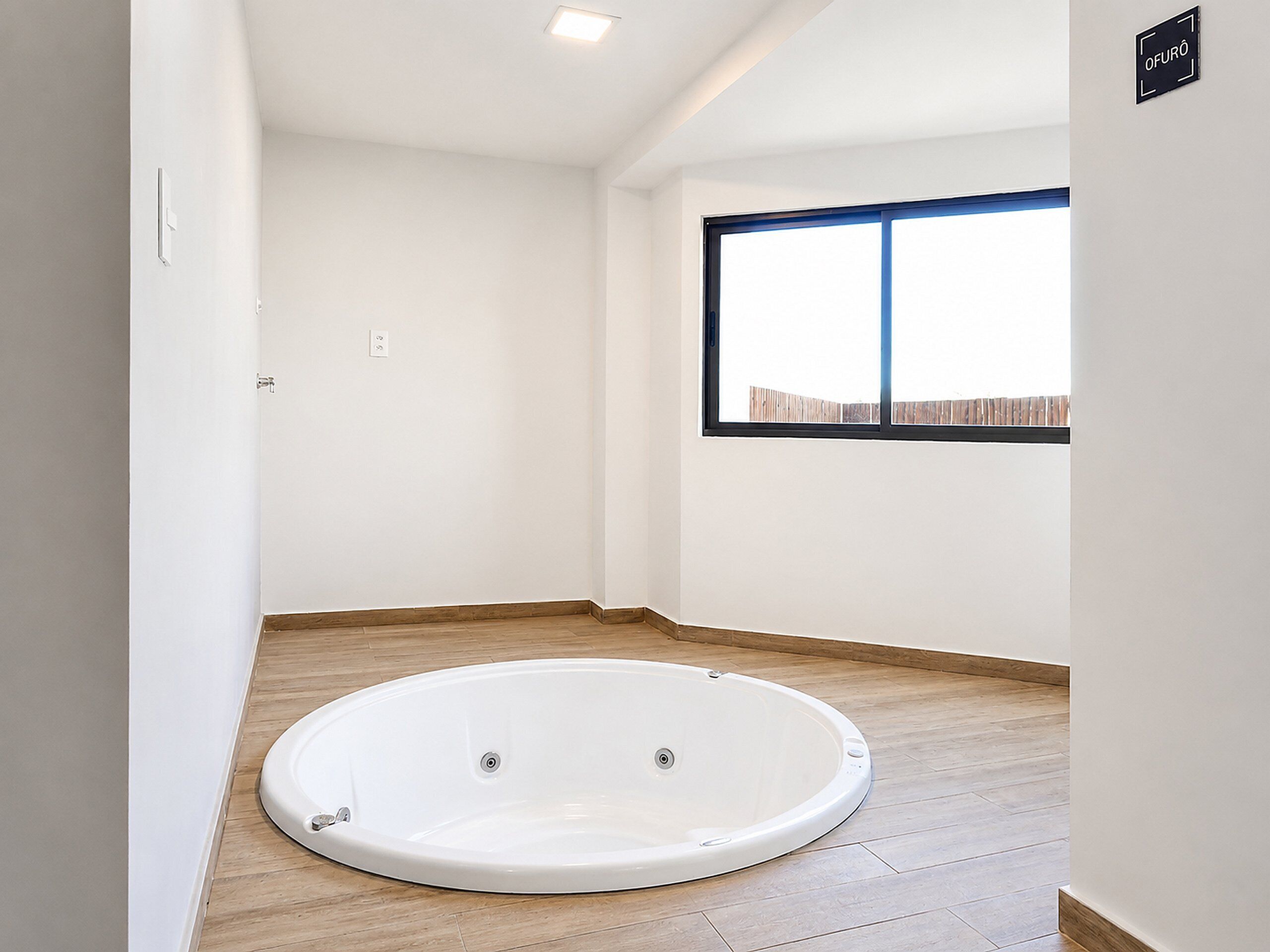 A room with a bathtub, wooden flooring, a window with a view, and a sign on the wall.
