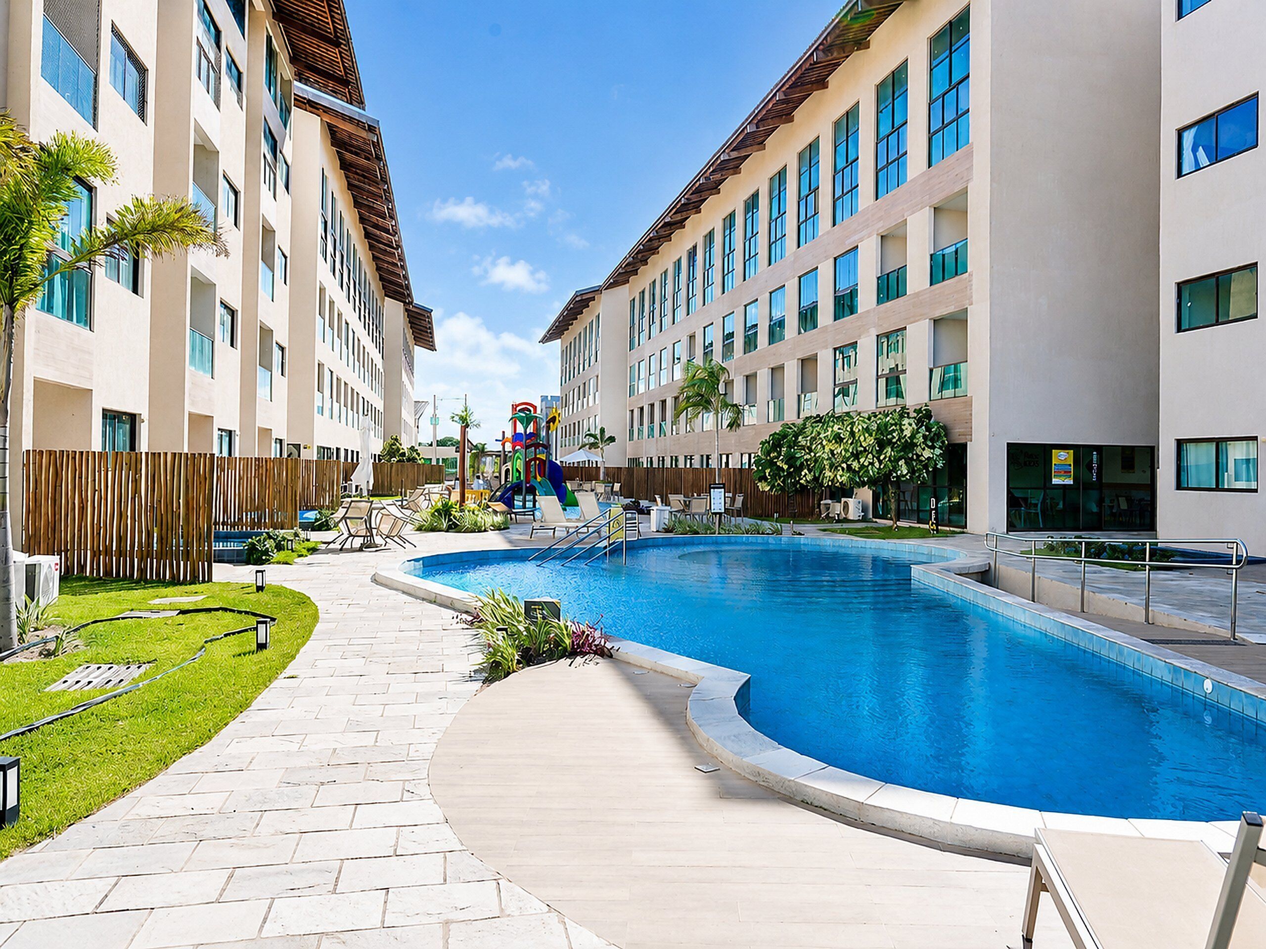 A swimming pool with a curved edge, surrounded by a paved walkway, and adjacent to a multi-story building with balconies.