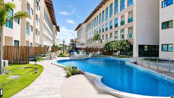 A swimming pool with a curved edge, surrounded by a paved walkway, and adjacent to a multi-story building with balconies.