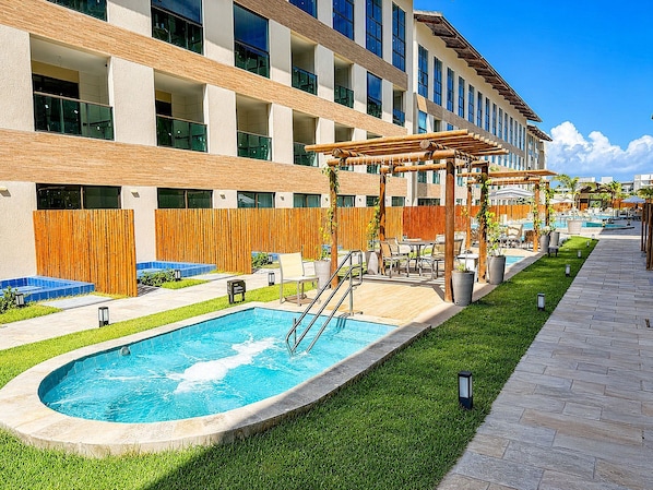 A hotel with a swimming pool, outdoor seating, and a pergola. - Hosts BR - MAX Carneiros Suítes (Tamandaré)