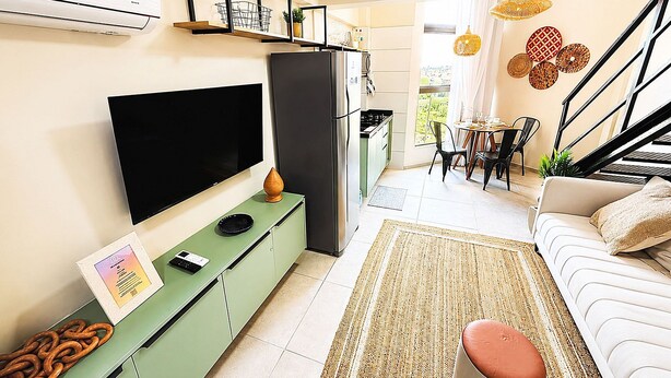 Una sala de estar moderna con un televisor de pantalla plana, un aparador verde, un sofá, un comedor y una escalera.
