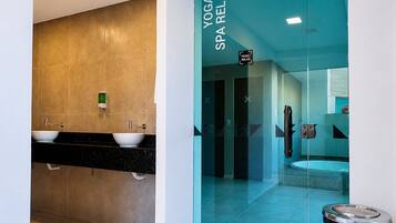 A modern bathroom with a glass partition, a sink with two basins, and a sign indicating a yoga and spa relaxation area.