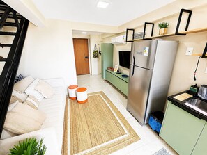 A modern kitchen with a stainless steel refrigerator, a green countertop, and a white sofa with orange cushions. - Hosts BR - MAX Carneiros Suítes (Tamandaré)