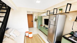Una cocina moderna con un refrigerador de acero inoxidable, una encimera verde y un sofá blanco con cojines naranjas.