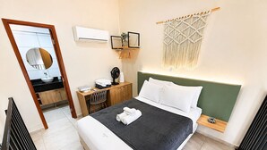 Un dormitorio con cama, escritorio, silla, espejo, aire acondicionado de pared y un tapiz de macramé.