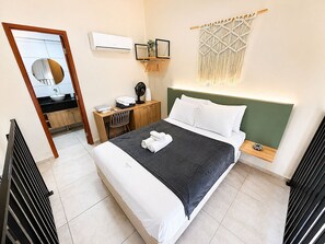Une chambre comprenant un lit, un bureau, une chaise, un miroir, un climatiseur fixé au mur et une décoration murale en macramé.