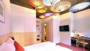 A hotel room with a bed, a desk, a TV, and colorful hanging lamps. - Barabas Hotel Luzern (Lucerne)