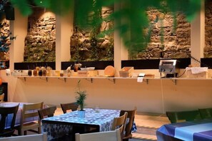 A restaurant with stone wall decor, tables with blue and white patterned tablecloths, and a variety of food items displayed on shelves. - Barabas Hotel Luzern (Lucerne)