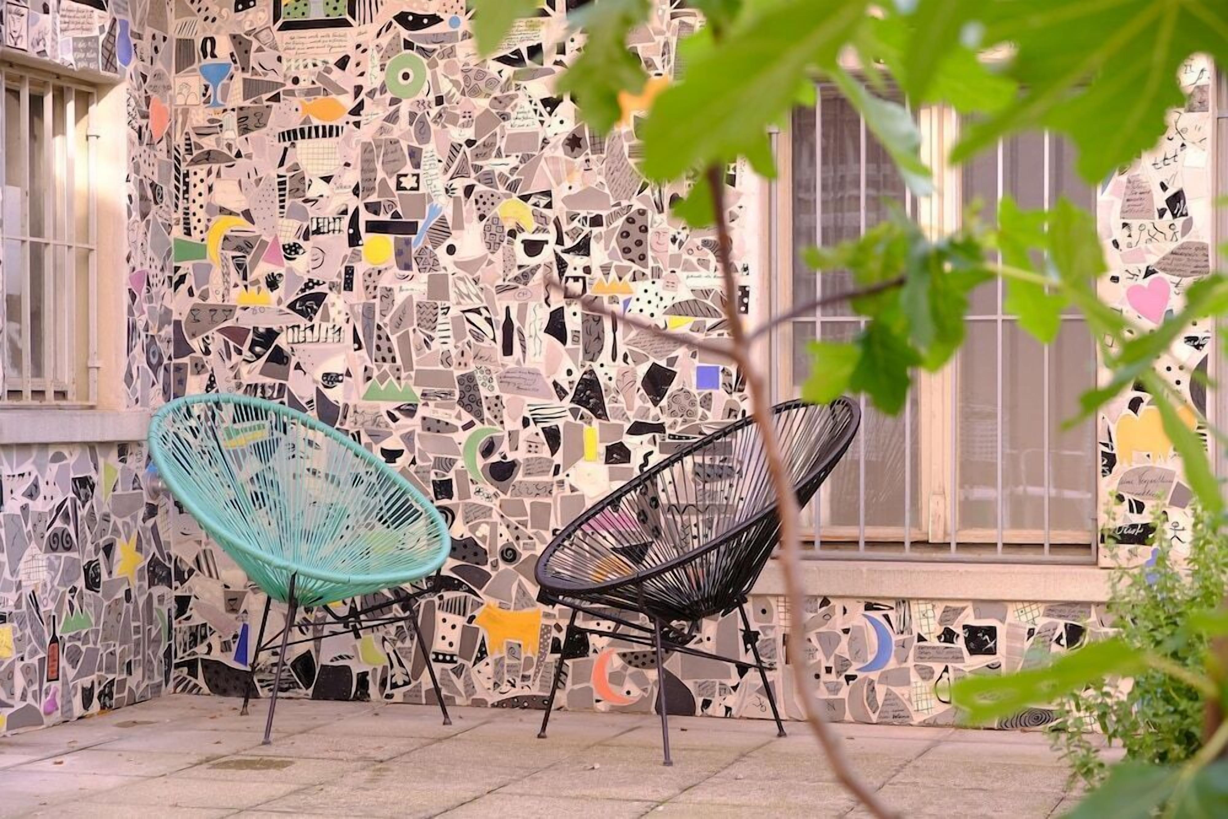 Un coin avec deux chaises, un mur recouvert de différents motifs et une fenêtre donnant sur un paysage.