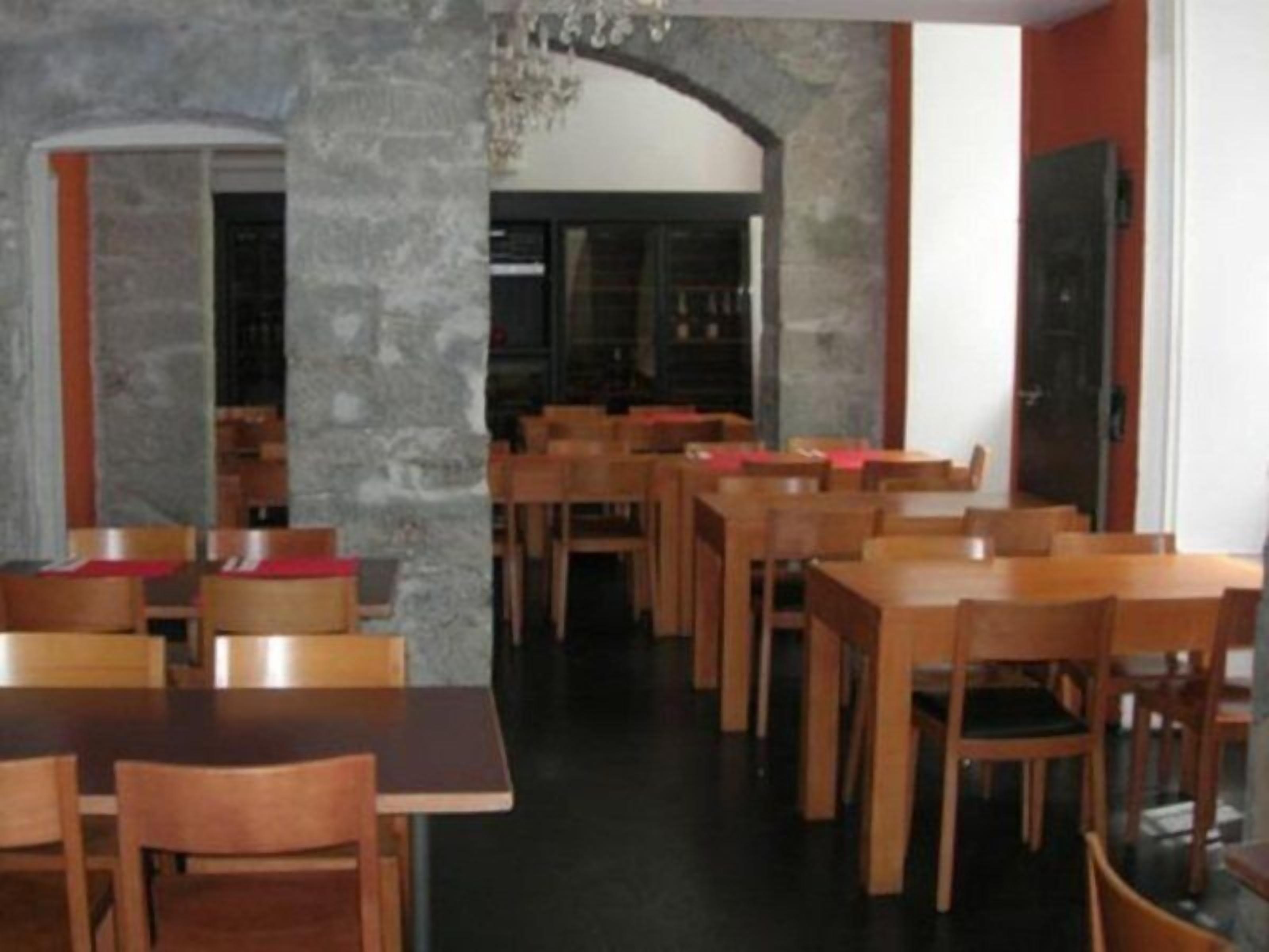 A restaurant with multiple wooden tables and chairs, stone walls, and a chandelier.