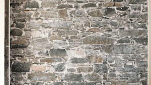 A room with a stone wall, a grey sofa with cushions, and wooden flooring. - Barabas Hotel Luzern (Lucerne)