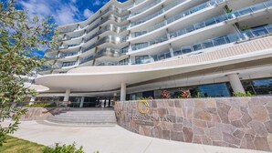 Een meerlaags hotel met een gebogen gevel, een stenen basis en een bord waarop 'The Cosmopolitan Cotton Tree' staat.