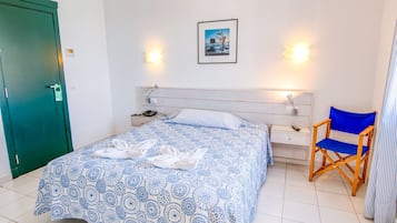 Uma cama bem arrumada com colcha estampada, mesa de cabeceira com abajur, uma cadeira e um quadro na parede.