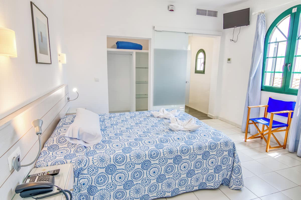 A hotel room with a bed, a desk, a chair, a wardrobe, and a TV.
