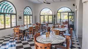 Un restaurante con piso a cuadros, mesas redondas, sillas de madera y ventanas arqueadas grandes.