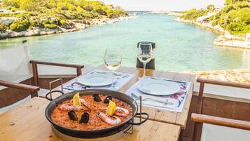 Una mesa con paella de mariscos, copas de vino y vistas a un paisaje costero.