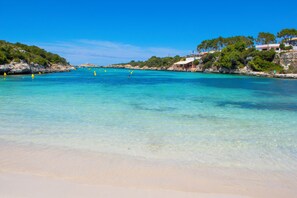 A beach with clear turquoise water, sandy shore, and rocky cliffs with vegetation.