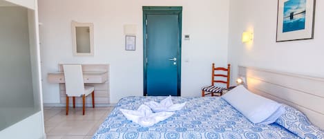 A bedroom with a bed, a desk, a chair, a door, and a wall-mounted light.