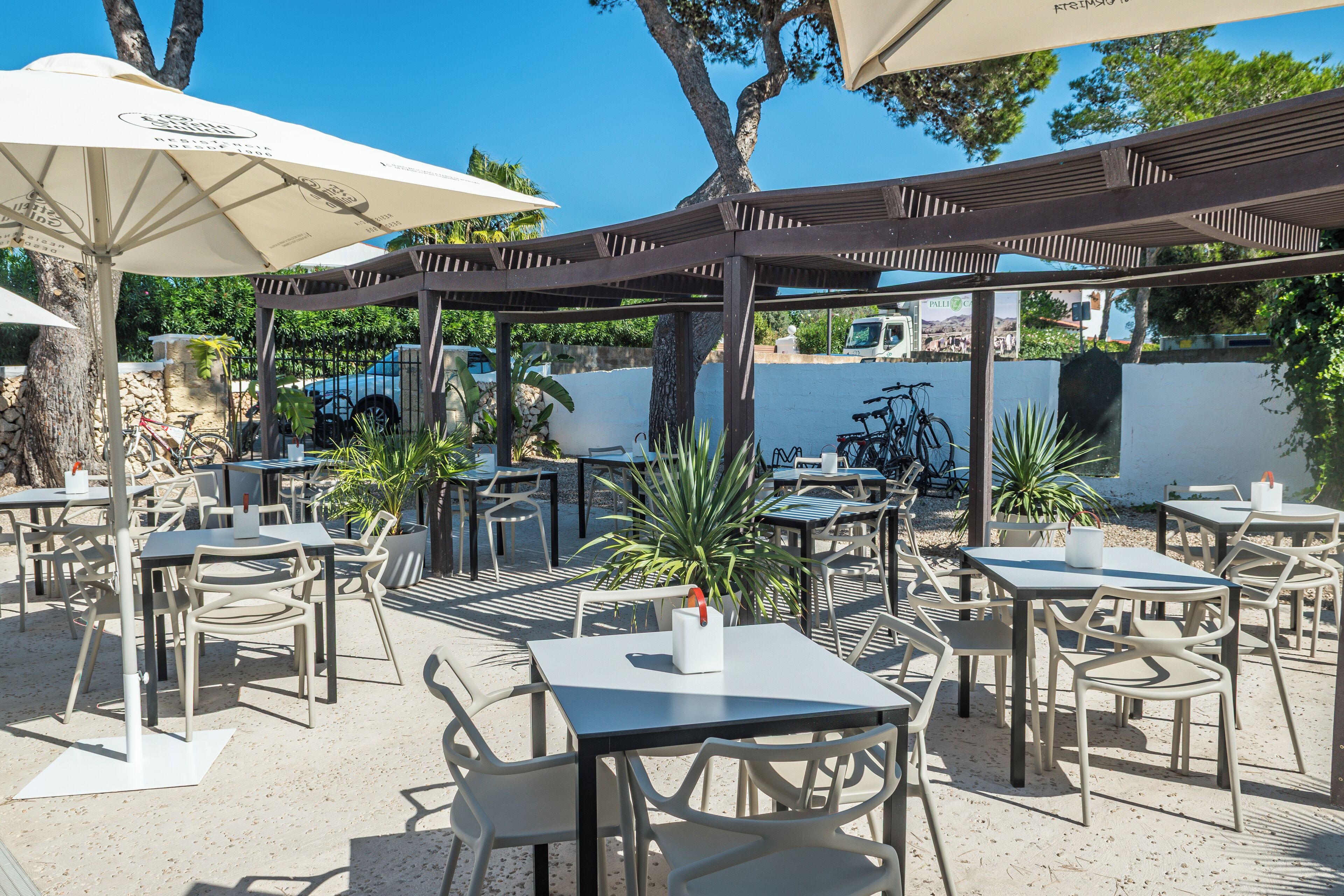 Un'area patio all'aperto con tavoli, sedie, ombrelloni e piante in vaso.