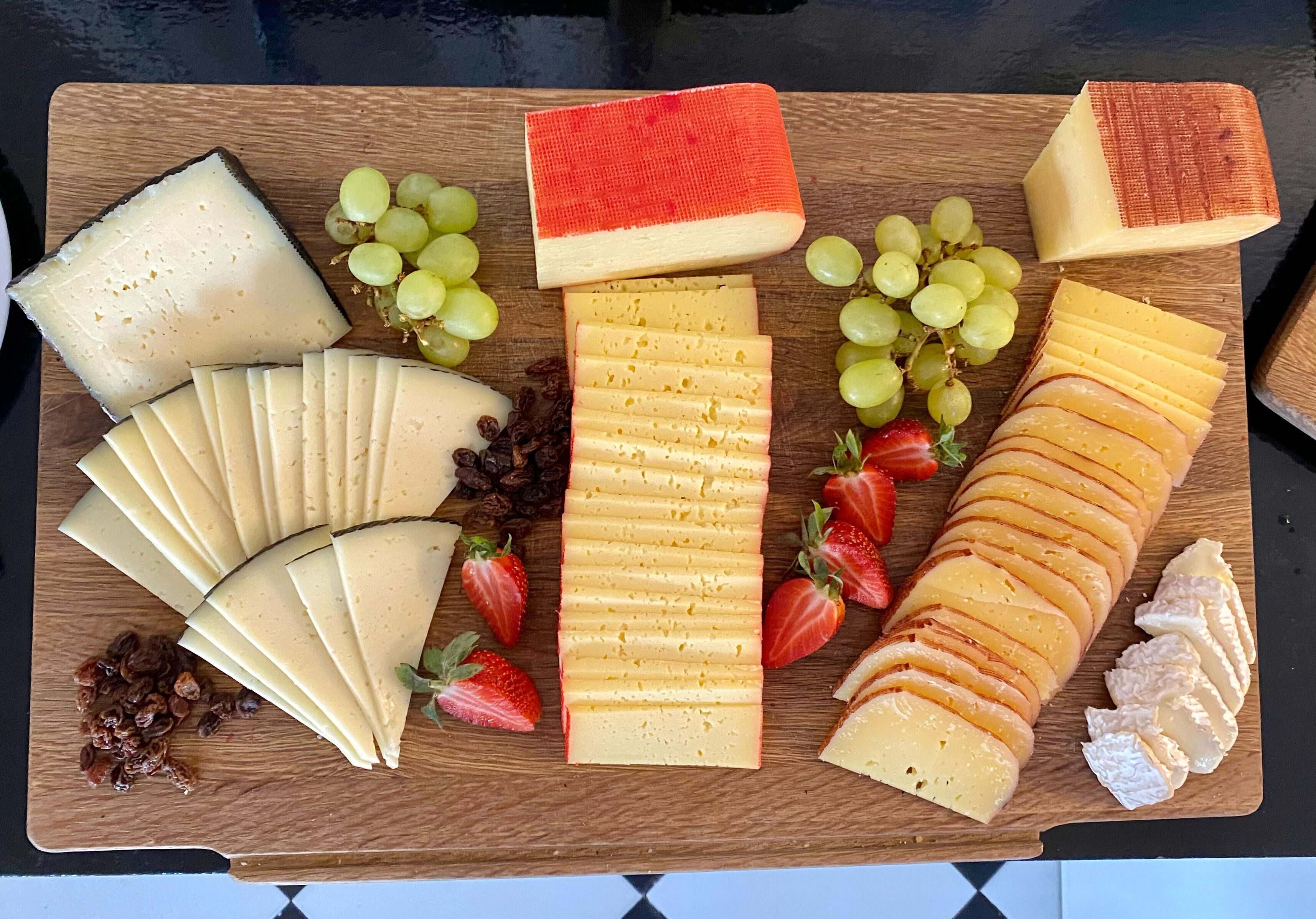 A variety of cheeses and grapes on a wooden board.