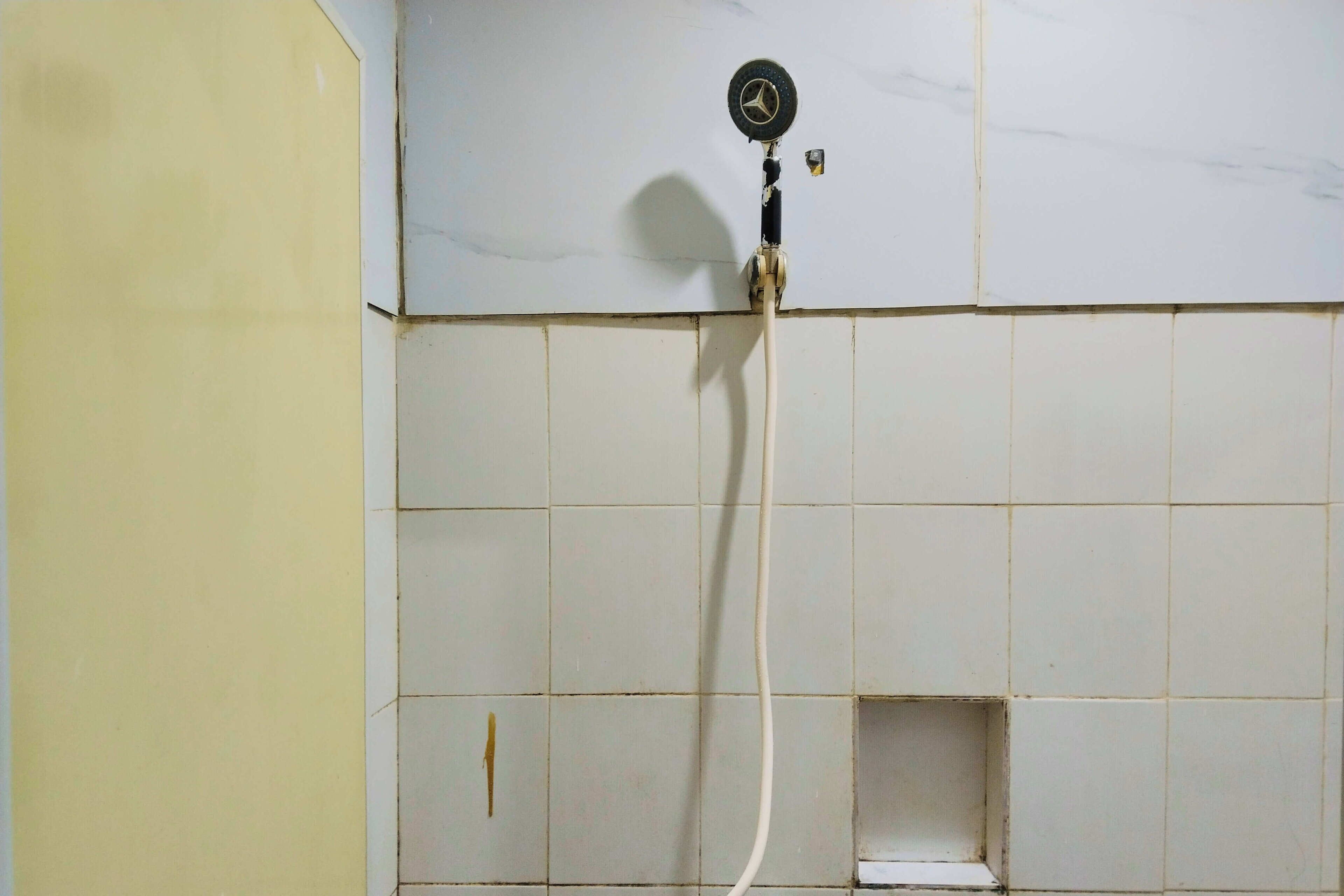 Baño con ducha, paredes de azulejos y una tubería de agua visible.
