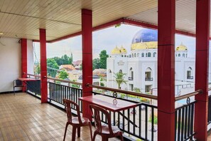 Un balcon doté d’un plancher en bois, de piliers rouges et offrant une vue sur un bâtiment blanc surmonté de coupoles dorées.
