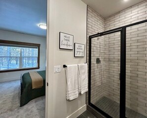 Ein Badezimmer mit Dusche, einem Bett und einem Fenster mit Blick auf Bäume.