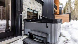 Ein modernes Gebäude mit einer Steinfassade, einem großen Whirlpool und einer Holzterrasse.